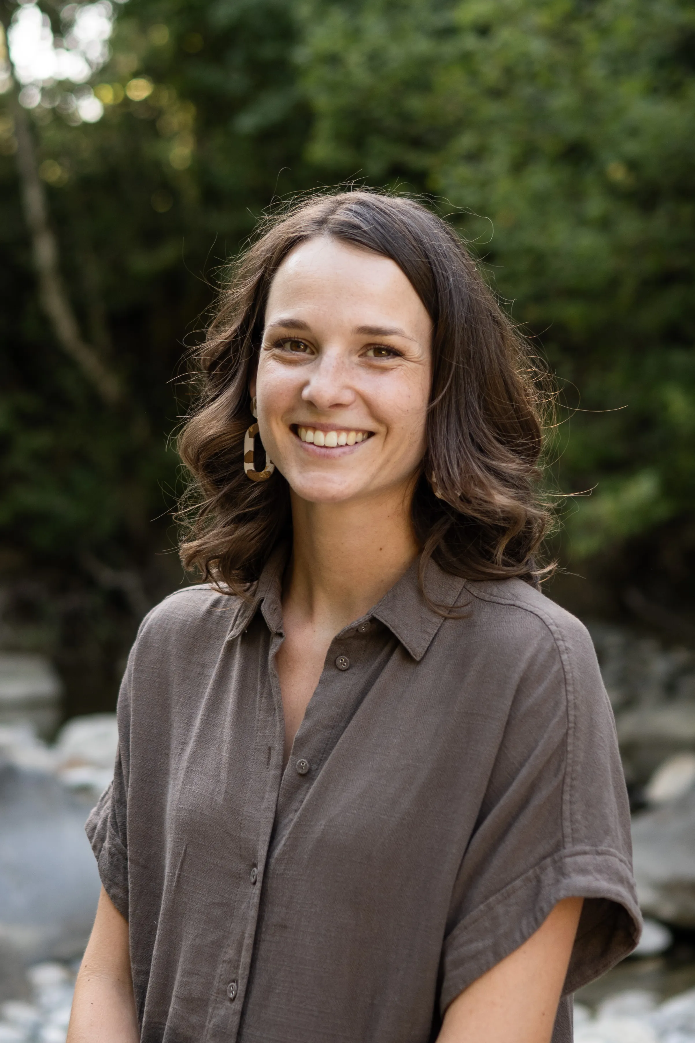 Portrait d’Estelle, praticienne en réflexologie et soins énergétiques, souriante en extérieur au bord d’une rivière
